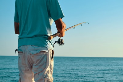 Man holding a fishing rod in the face of blue ocean
